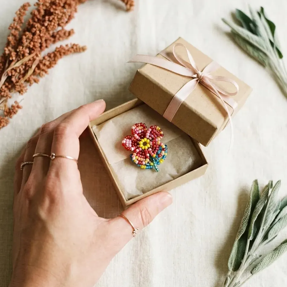 A handmade beaded flower brooch in a small gift box